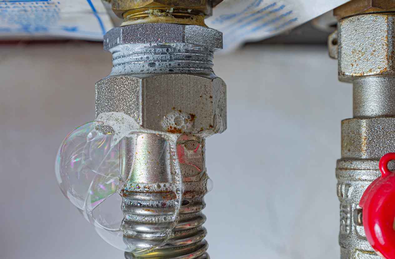 Gas leak at home heating boiler. Inflating bubbles of soap mixture applied to the threaded joint on the gas flexible pipe indicate a gas leak.